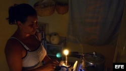Una mujer prepara unos platos de comida en la cocina, iluminada con velas, en un apagón en el barrio de Alamar