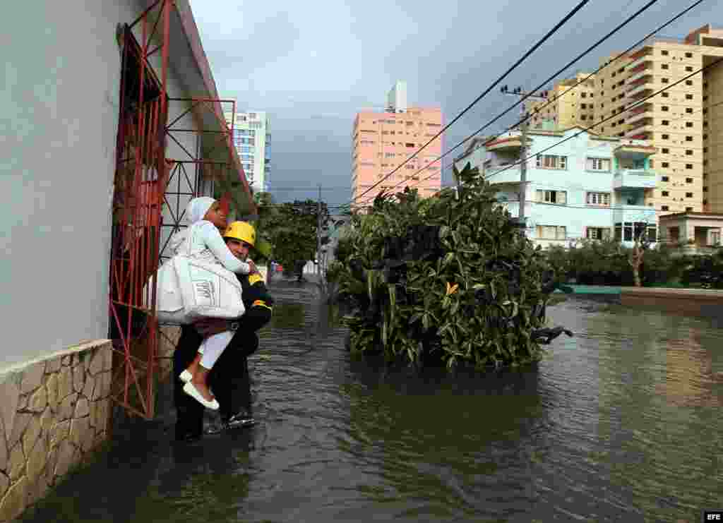 El bombero del destacamento de Rescate y Salvamento Ángel Games carga a una mujer por una calle inundada por las penetraciones del mar hoy, sábado 23 de enero de 2016, en La Habana (Cuba). EFE/Alejandro Ernesto