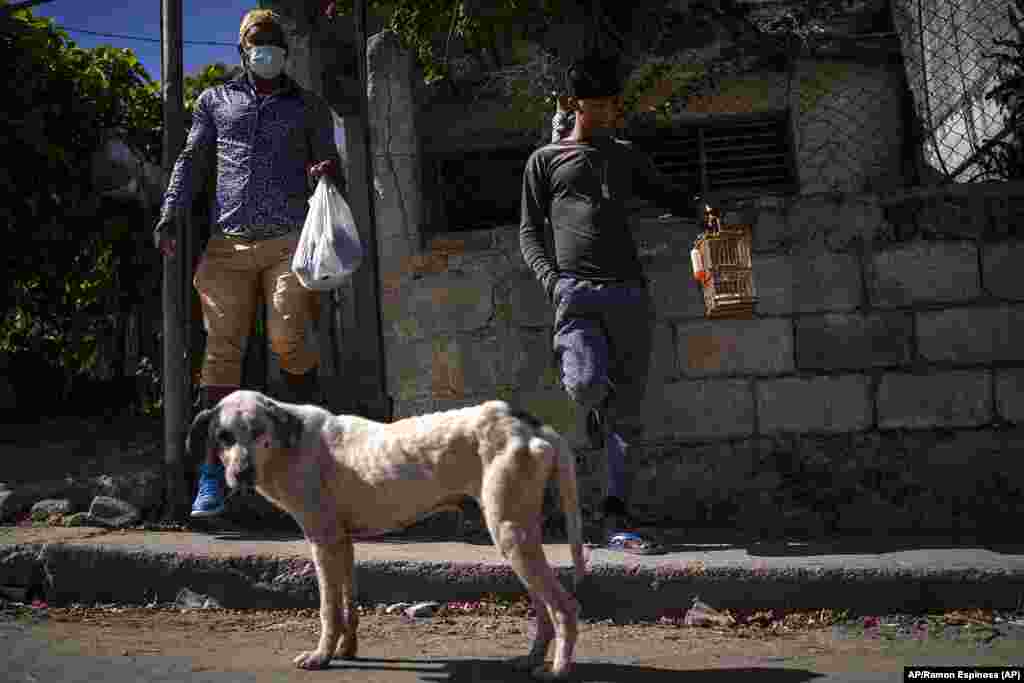 Odlanier Santiago Rodríguez (al centro), acusado de participar en protestas pasadas y excarcelado tras 22 días de prisión, espera junto a la puerta de su casa con su tío Emilio Román, quien tiene a sus tres hijos presos por el mismo motivo, en La Güinera