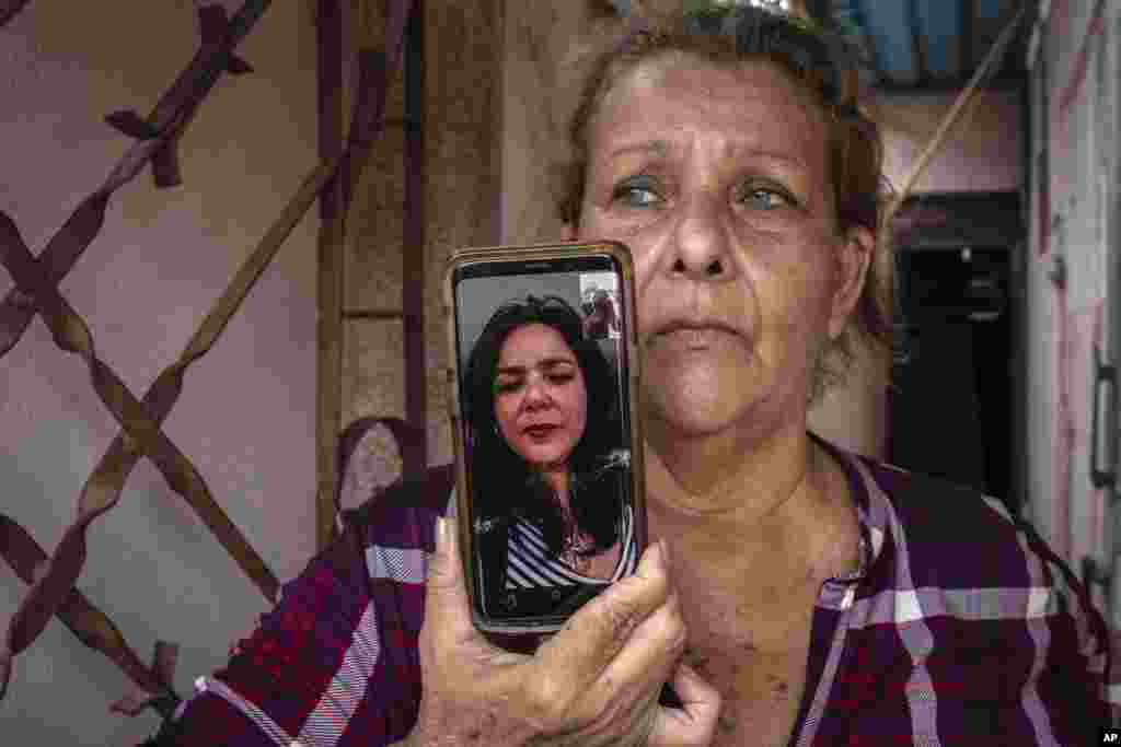Yanelis Leon habla por videollamada desde Estados Unidos durante una entrevista mientras su madre, Natacha González, quien cuida de sus dos hijos, sostiene el celular en la entrada de su casa en Cienfuegos.  (AP Foto/Ramón Espinosa)