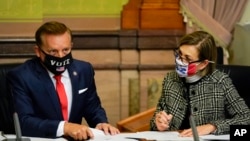 El secretario de Estado de Iowa, Paul Pate, a la izquierda, y la gobernadora de Iowa, Kim Reynolds, cuentan los votos emitidos por los miembros del Colegio Electoral de ese estado.